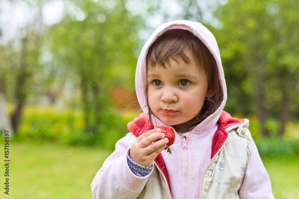 Little girl in a hoodie eating strawberries Little girl in a hoodie eating strawberries