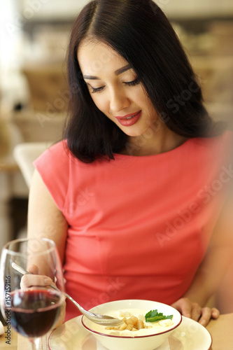 Woman having dinner in restaurant. Portrait of girl in red dress eating and drinking red wine