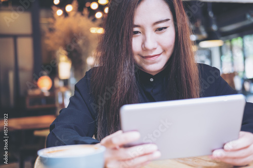 A beautiful Asian woman with smiley face using tablet in modern cafe