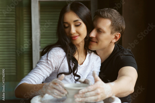 Romantic caucasian couple working on potter whel. Handsome man and pretty beautiful brunette woman making and sculpting clay pot together and hugging photo