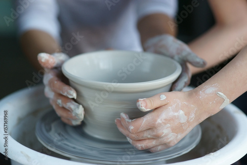 Mother teaches son to work on pottery wheel. Close up of dirty hands sculpting clay.