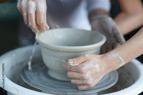 Mother teaches son to work on pottery wheel. Close up of dirty hands sculpting clay.