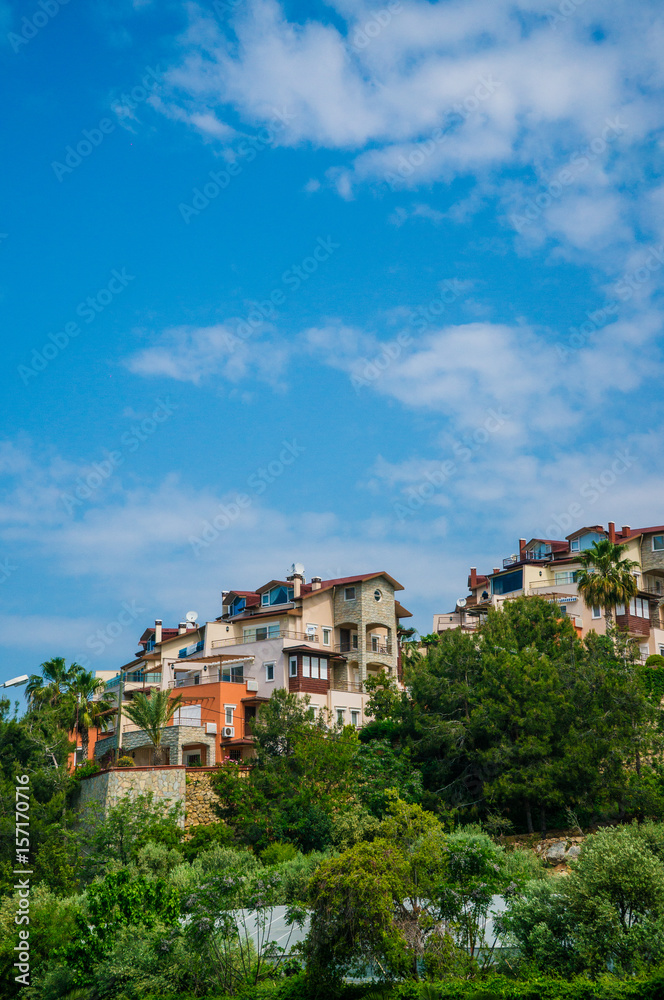 Residential two-storey houses on the slope of the mountain. The village is against the blue sky among the green trees.