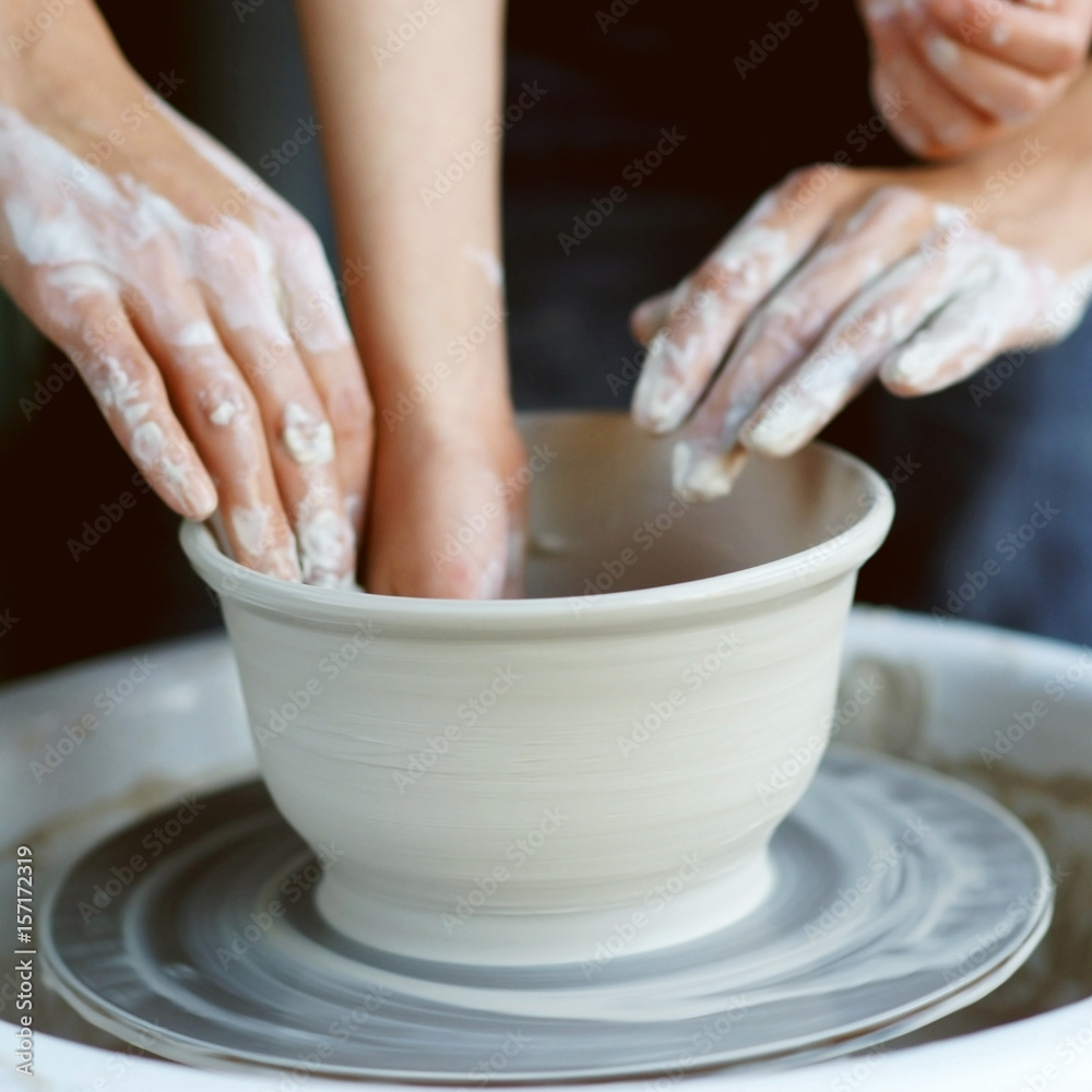 Mother teaches son to work on pottery wheel. Close up of dirty hands sculpting clay.