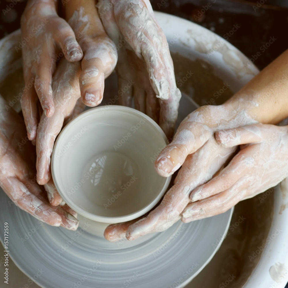 Family working on pottery wheel. Top view of mother, father and son hands making ceramic pot or sculpting clay Family working on pottery wheel. Top view of mother, father and son hands making ceramic pot or sculpting clay