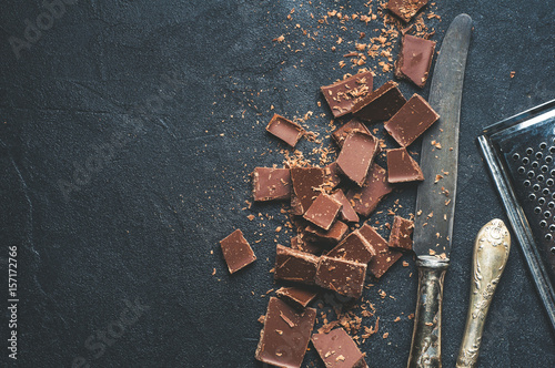 The chunks of chocolate and antique knives over dark concrete background