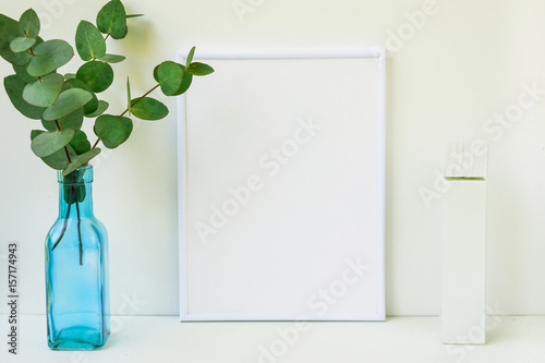 Frame mockup on white background, green eucalyptus branch in blue glass bottle, copyspace, blank tube, product marketing photo