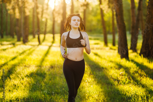 Fototapeta Naklejka Na Ścianę i Meble -  Fitness girl running on nature while listening music with headphones. Fitness concept. Sunset backgroung.
