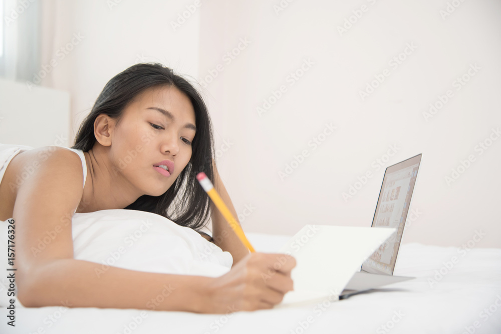 Asian girl writning on notebook with laptop on her bed. Asian girl writning on notebook with laptop on her bed.