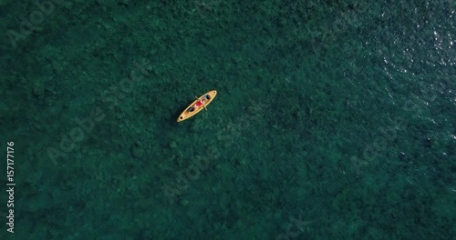 Silhouette of tiny blonde female in bright red one piece swimsuit resting on top of yellow kayak, cruisng through crystal clear waters of mediterranean sea photo