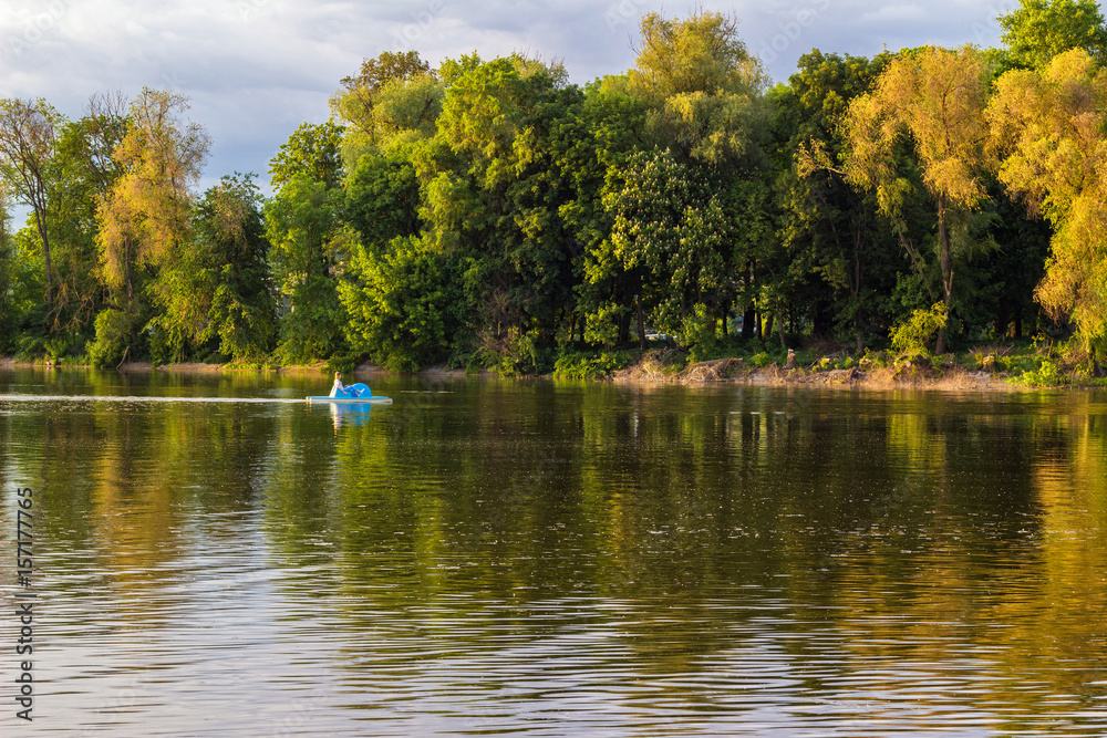 Trees reflection on the river, people resting on small catamaran on the water
