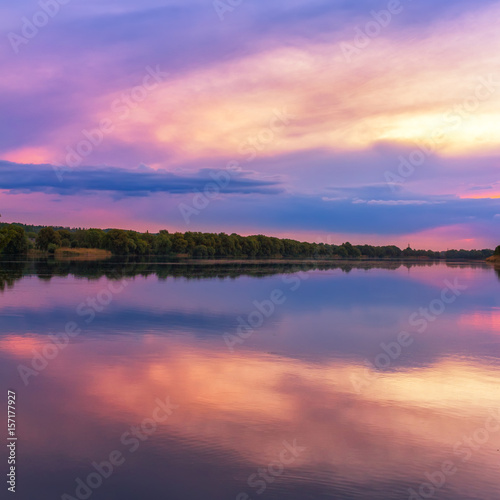 Vivid scenery of sunset at the river, colorful, dramatic evening sky reflected in the water, hdr image. Khmelnytskyi, Ukraine