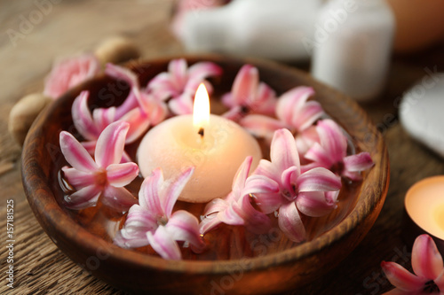 Bowl with water  hyacinth flowers and burning candle on wooden table  closeup