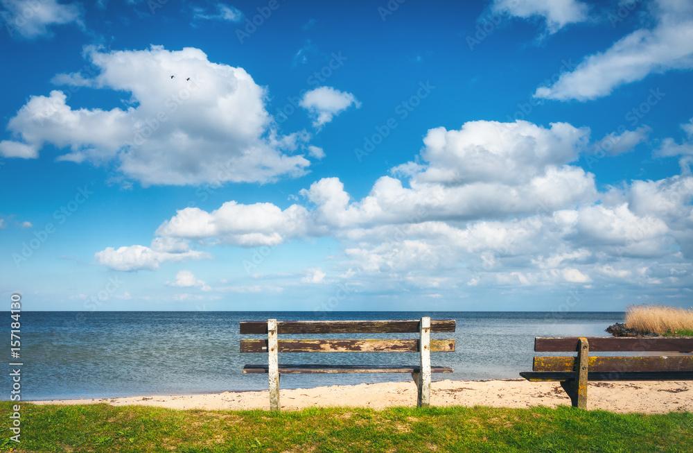 Bench on the sandy beach at the sea on the background of colorful blue sky with clouds at sunset. Beautiful landscape with empty old wooden bench standing on sea coast in the evening in Netherlands