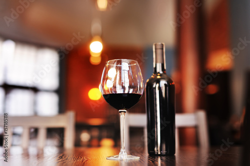a glass of red dry wine with a bottle on a table