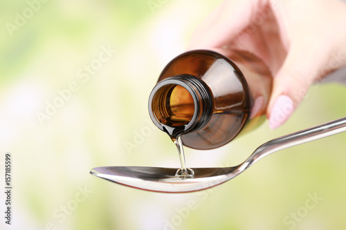 Pouring cough syrup into spoon on blurred background