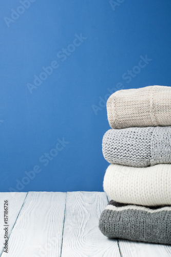 Knitted wool sweaters. Pile of  winter clothes on blue wooden background, , knitwear, space for text. © lana_u