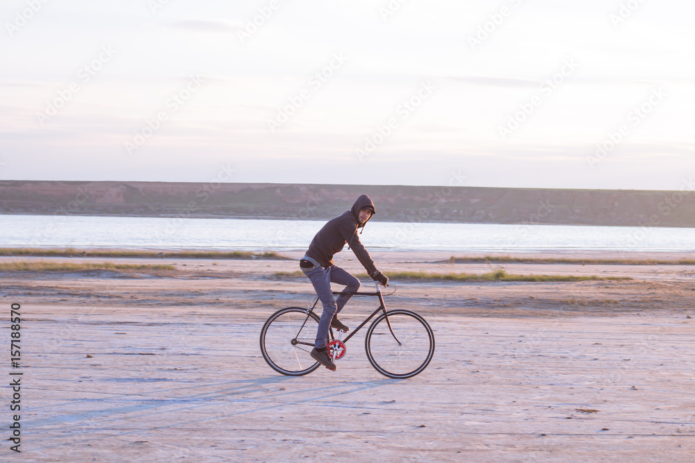 Obraz premium Alone rider on fixed gear road bike riding in the desert near river, hipster tourist bicycle rider pictures.