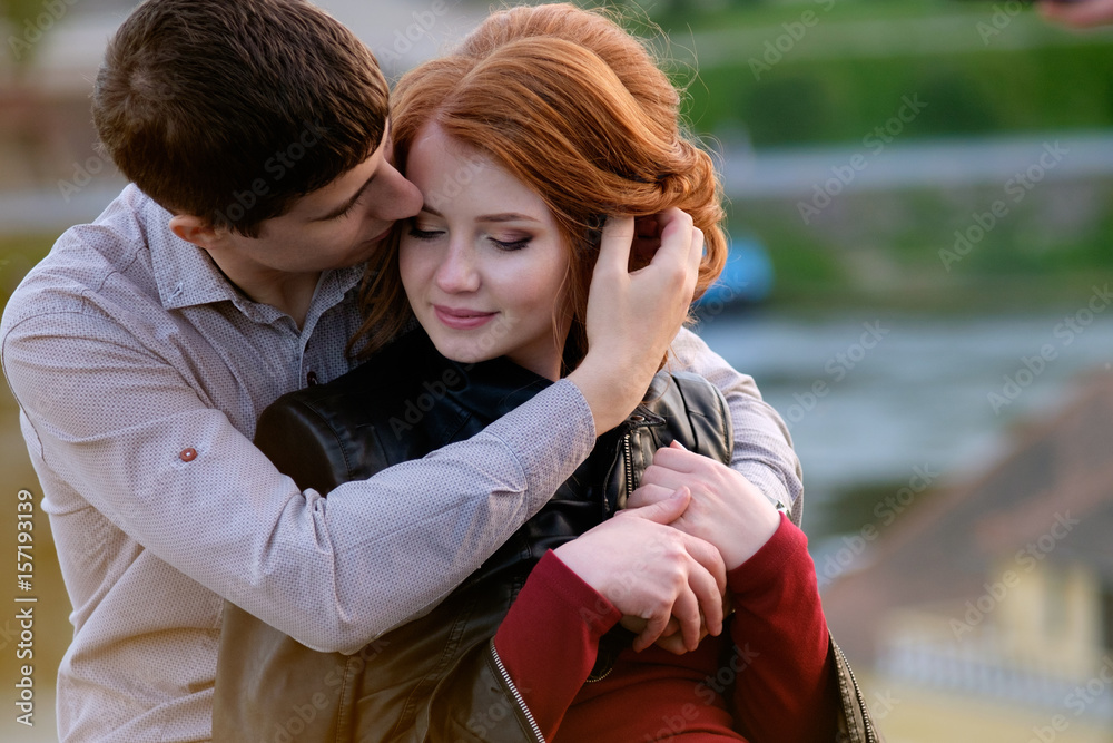 Redhead pretty girl in hugs of handsome brunette man, romantic moment