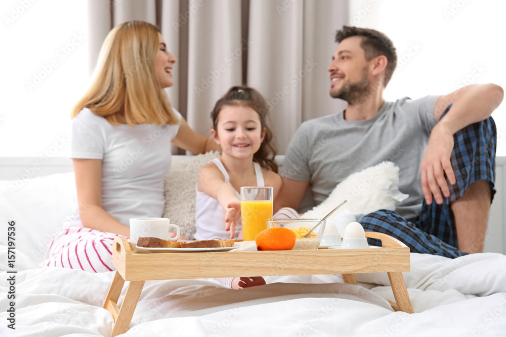 Happy family sitting on bed with breakfast