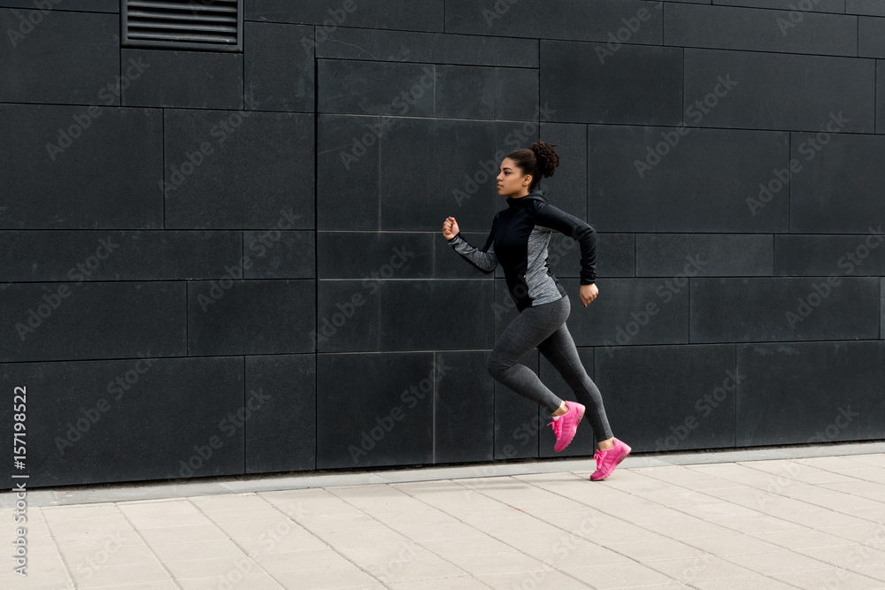 Side view of female athlete running near a wall Side view of female athlete running near a wall