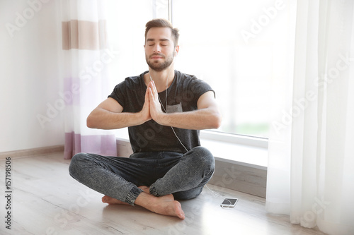Young man practicing yoga near big window