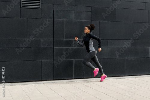 Side view of female athlete running near a wall