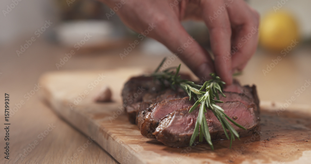 man decorating sliced medium rib eye steak with rosemary branch, wide photo