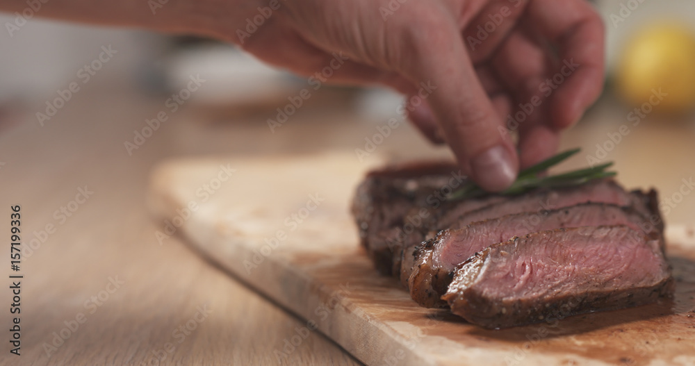 man decorating sliced medium rib eye steak with rosemary branch, wide photo