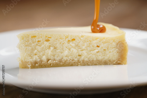 caramel sauce pour on cheesecake on plate closeup, shallow focus