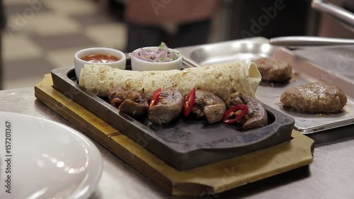 A cook decorates a dish with meat and pita bread in a metal tray. Before serving a hot meal, the chef of the restaurant completes the decoration with pieces of red pepper lulia kebab. On the cast-iron photo