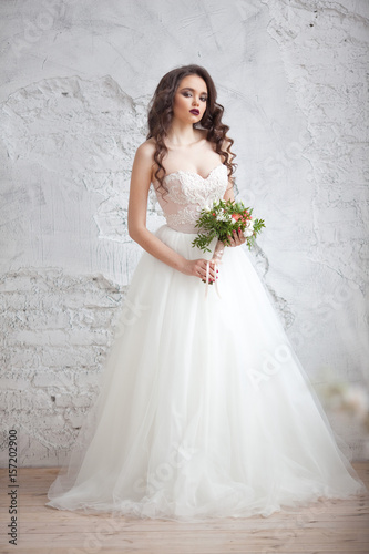Portrait of a beautiful young girl of European appearance in a stylish white wedding dress with a hairdo and makeup with a wedding bouquet in the hands of fine flowers