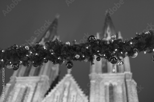 Decorative christmas ornaments (baubles) on evergreen girlands  at the outdoor christmas markets in Prague, Czech republic, with the church of Saint Ludmila in the background, in black and white photo