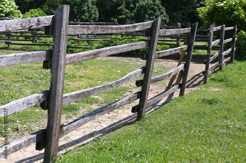 Brown country style fence dividing a green grassy pasture