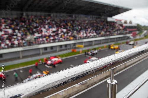 Racing cars on the starting grid. The focus on the handrail with rain drops