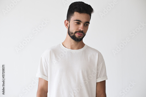 Portrait of serius dreamy attractive young male model wearing simple but stylish and fashionable simple white t-shirt on isolated mock up wall photo