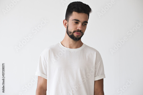 Portrait of serius dreamy attractive young male model wearing simple but stylish and fashionable simple white t-shirt on isolated mock up wall