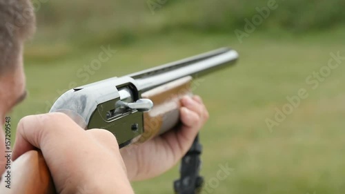 Closeup shot of a man training in competitive and recreational skeet shooting from a modern smoothbore shotgun with flying away cartridge in a green field in a sunny day in slow motion