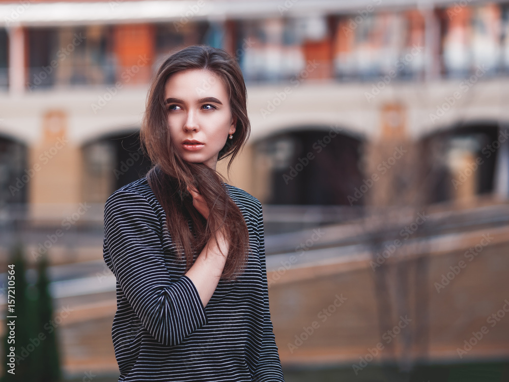 Young attractive caucasian girl or woman in striped dress over blurred city background