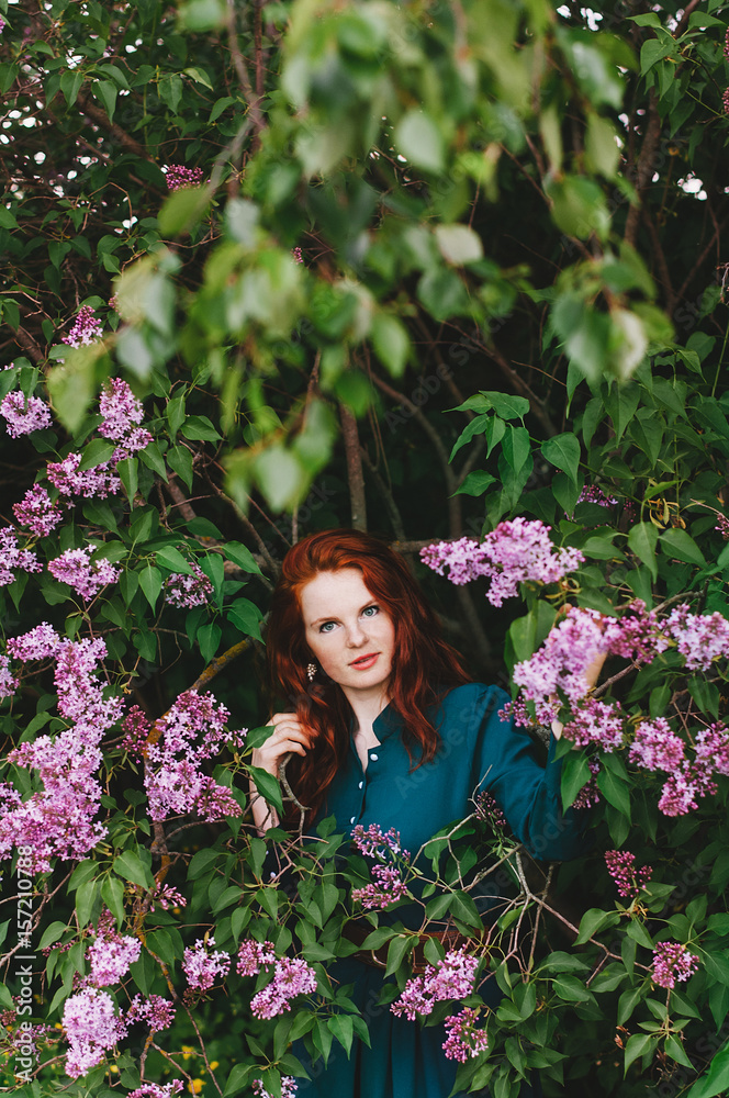 The red-haired girl is standing near the lilac bush The red-haired girl is standing near the lilac bush