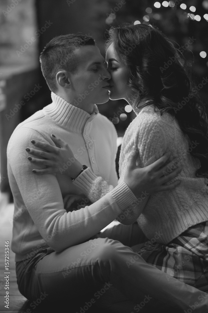 Young couple staying at home together on holiday evening and sitting on floor in front of christmas tree and hugging. Cute romantic lovers in white pullovers Young couple staying at home together on holiday evening and sitting on floor in front of christmas tree and hugging. Cute romantic lovers in white pullovers