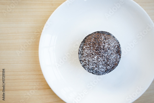 Chocolate muffins with sprinkled icing sugar on a white plate and wooden table