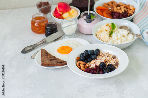 Healthy breakfast - granola with blackberry, dry cranberry, blueberry, almond, cottage cheese with banana, fried eggs with bread, yogurt,  jams, nuts, sour cream on a white background.