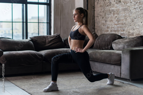 Pretty fit woman doing frontal lunges or squat exercise indoors in a flat photo