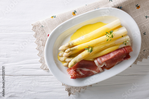 White asparagus with hollandaise sauce and ham close-up on a plate. Horizontal top view