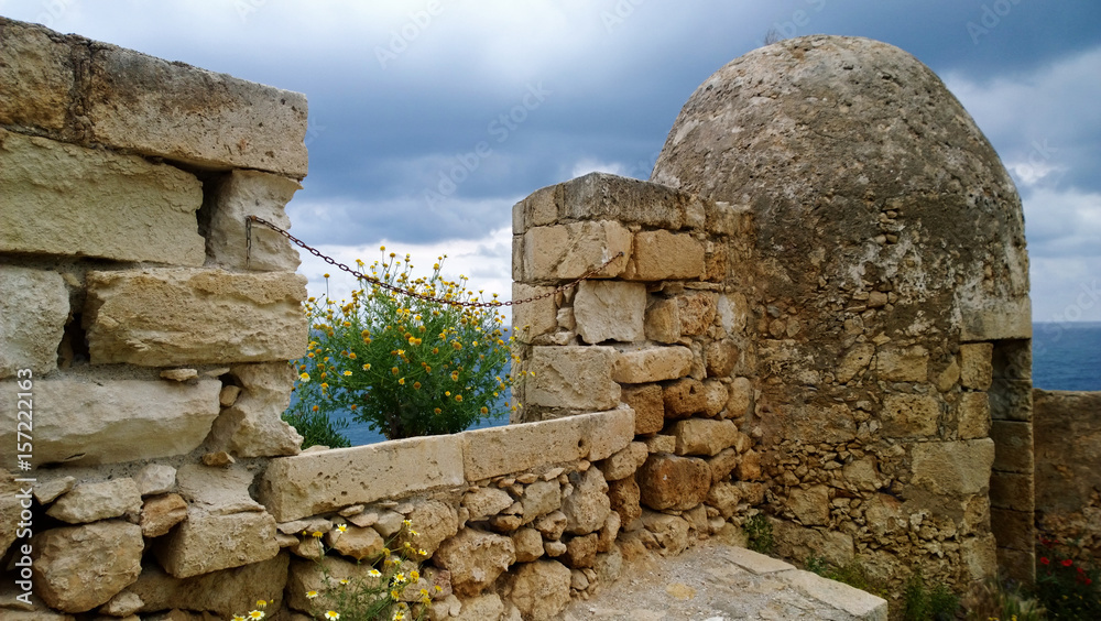 Part of the destroyed wall in the city of Rethymno with flowering daisies in spring day