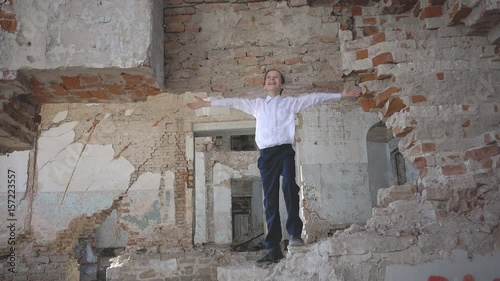 The boy in the ruined building spread his hands to the side and looks up into the sky