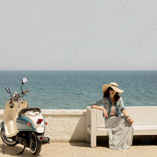Young beautiful woman in a long skirt sits on a bench on the waterfront.