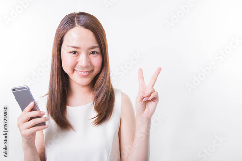 Portrait of a smiling woman holding a smartphone and peace sign gesture