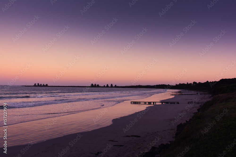 Long sandy beach at sunset with purple skies and water